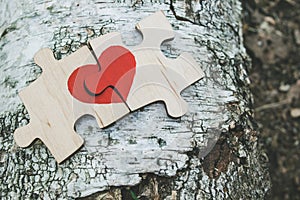 Red heart is drawn on the pieces of the wooden puzzle lying next to each other on wooden background. Love concept. St. Valentine