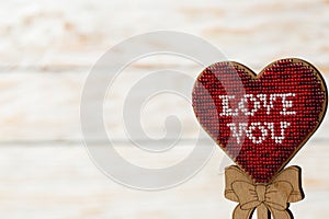 Red heart embroidered of beads on a wooden white background. The concept of Valentine`s Day.