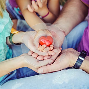 Red heart in family hands on bright background