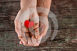 Red heart in female hand on wooden background