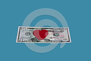 Red heart on a fifty dollar bill isolated on a blue background.