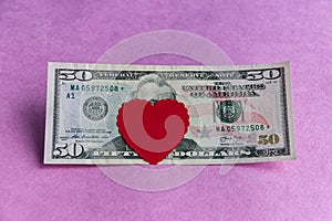 Red heart on a fifty dollar bill on a pink background. Close-up.