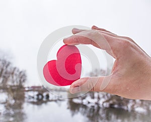 Red heart in the hand of the girl. river background