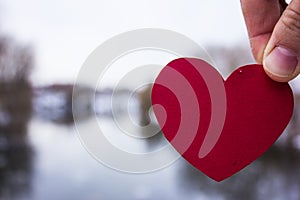 Red heart in the hand of the girl. river background