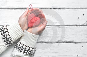 Red heart in the hands of a young woman in a white wool sweater with an ornament on a white wooden rustic background. Valentine`s