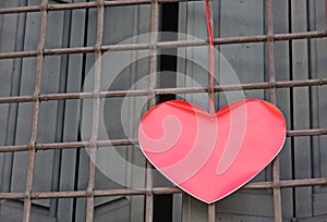 Red heart hanging on the grid of a window outside a building on