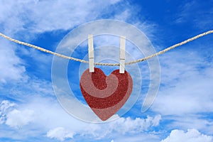 Red heart hanging on a hemp rope on the blue sky background