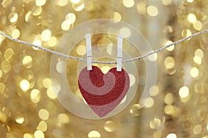 Red heart hanging on a hemp rope on the gold bokeh background