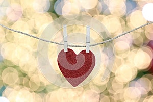 Red heart hanging on a hemp rope on the gold bokeh background