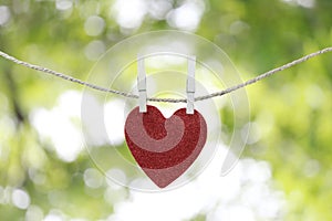 Red heart hanging on a hemp rope on the green bokeh background