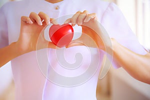 Red heart held by smiling female nurse`s hand, representing giving effort high quality service mind to patient. Professional, Spec