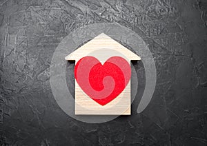Red Heart inside a wooden house on a gray concrete background. The concept of a love nest, the search for new affordable housing