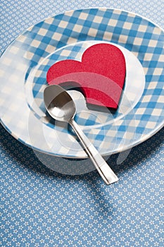 Red heart lying on blue vintage plate with spoon