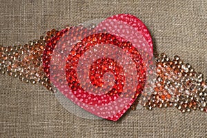 Red heart with many beads on rough fabric