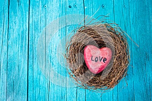 Red heart in nest and turquoise wooden background in country style.