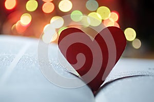 Red heart on an open book page with colorful bokeh lights background. Copy space.