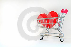 A red heart pillow in pink mini shopping cart on wooden table on