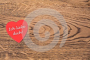 Red heart post-it with the text `Ich liebe dich` on a wooden background. Translation: `I love you`