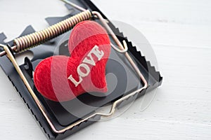 Red heart in a rat trap on white wooden background. Online internet romance scam or valentine day in darkside concept.