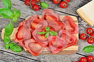 Red heart ravioli with tomato, mozzarella and basil on a wood background