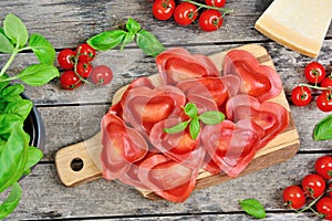 Red heart ravioli with tomato, mozzarella and basil on a wood background