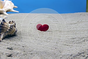 Red heart shape with seashells on the sandy beach. Selective focus on the heart