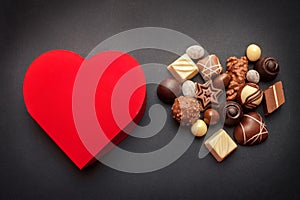 Red heart shaped box with chocolate pralines on dark background