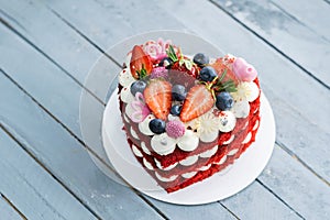 Red heart shaped cake decorated with white whipped cream slices of fresh strawberries . Concept of Valentine`s day