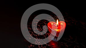 A red heart-shaped candle burns on a dark background. Copy space.