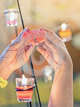 A red heart shaped candle in a woman`s hand with candlelight in many small glass cups.