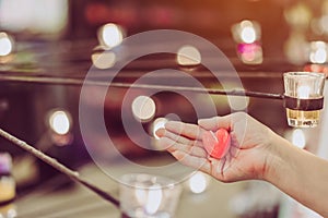 A red heart shaped candle in a woman`s hand with candlelight in many small glass cups.