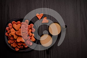 Red heart-shaped cookies and two mugs of coffee with milk on a black table. Valentine's Day