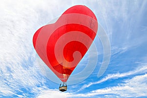 Red heart-shaped hot air balloon flying over a blue sky