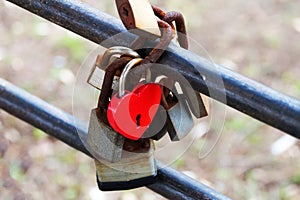 A red heart-shaped lock as a symbol of eternal love hangs on the railing with other locks