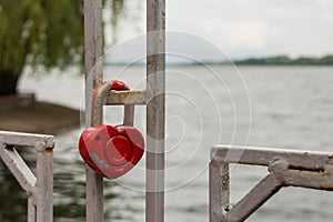 Red heart-shaped padlock on the fence on the background of the lake