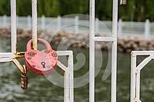 Red heart-shaped padlock on the fence on the background of the lake