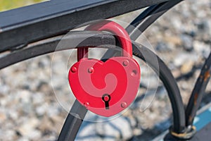 Red heart-shaped pendant lock hanging from the fence as a symbol of marriage