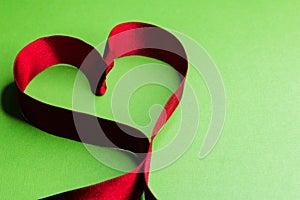 A red heart shaped ribbon on a green background can be used as a card background or Wallpaper for Valentine`s Day