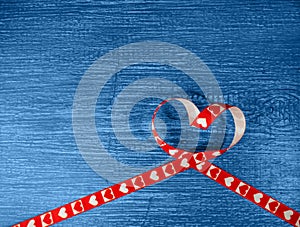 Red heart-shaped ribbon on an old, wooden blue background. Symbol of love