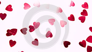 Red heart-shaped sequins are spinning in a circle on a pink background