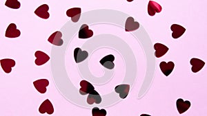 Red heart-shaped sequins are spinning in a circle on a pink background