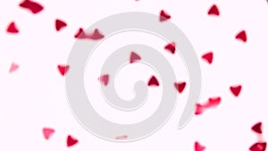 Red heart-shaped sequins are spinning in a circle on a pink background