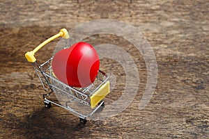 Red heart in shopping cart on wooden table.