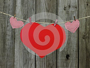 Red heart sign and striped fabric hearts hanging on clothlesline by shabby wooden background