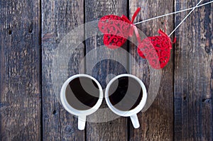 Red heart on a stick and two white cups with tea or coffee. On a wooden table