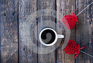 Red heart on a stick and a white cup with tea or coffee. On a wooden table. View from above