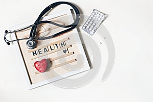 Red heart stone, stethoscope, wooden letter board and pills on white table background. Medical examination, treatment