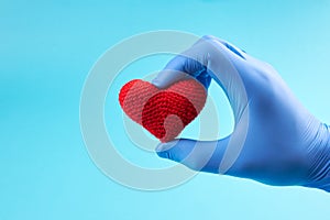 red heart symbol at persons hand with blue medical gloves on. light blue background with copy space. heart disease