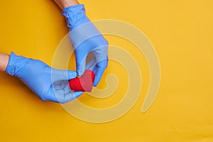 red heart symbol at persons hand with blue medical gloves on. yellow or orange background with copy space. heart disease