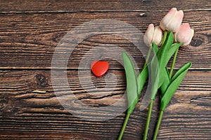 Red heart and three pink tulips on a brown wooden background. The concept of the holiday of Valentine`s Day, and International